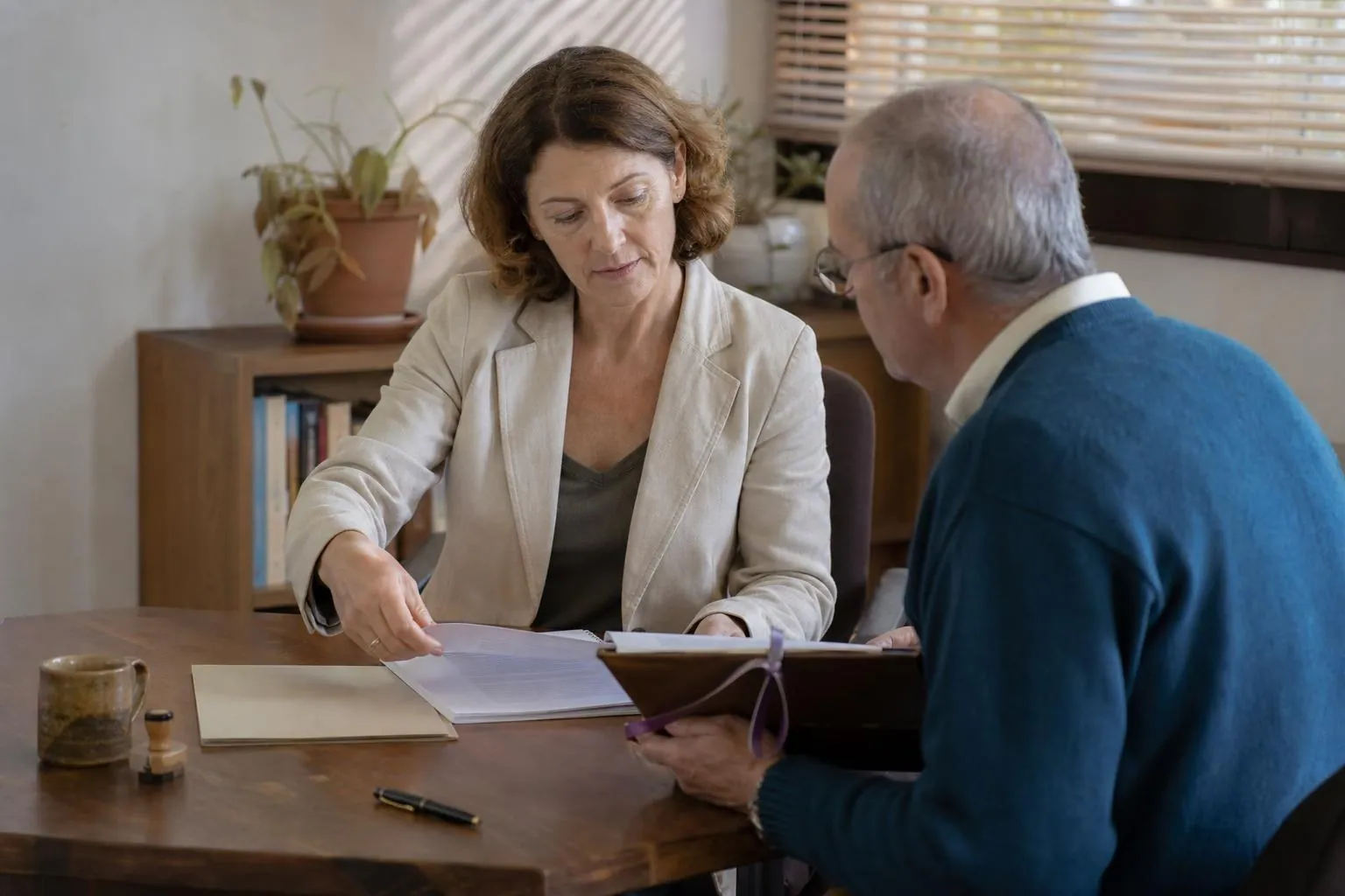 Une directrice d’association et un trésorier relisent une convention de subvention imprimée et reliée, posée à plat sur un bureau avec un parapheur ouvert